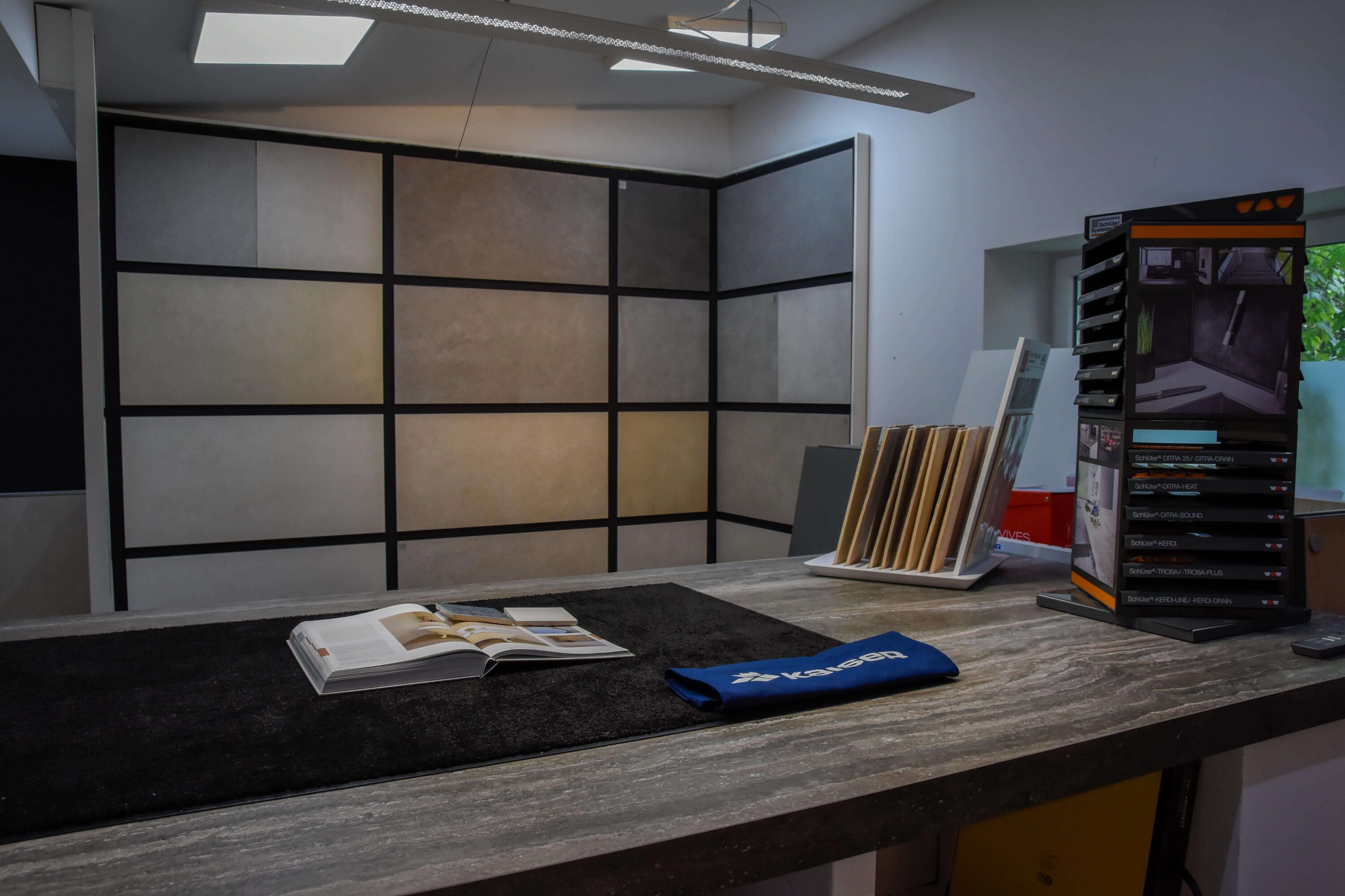 Fliesenausstellung von Kaiser Fliesenverlegebetrieb GmbH. Fliesenausstellung mit Fliesen an der Wand und Tresen, um Fliesenauswahl mit Kunden zu besprechen. Individuelle Fliesen zum Ansehen, Anfassen und für die persönliche Beratung direkt vom Chef. Kaiser Fliesenverlegebetrieb ist Ihr Fliesenleger aus Düsseldorf.